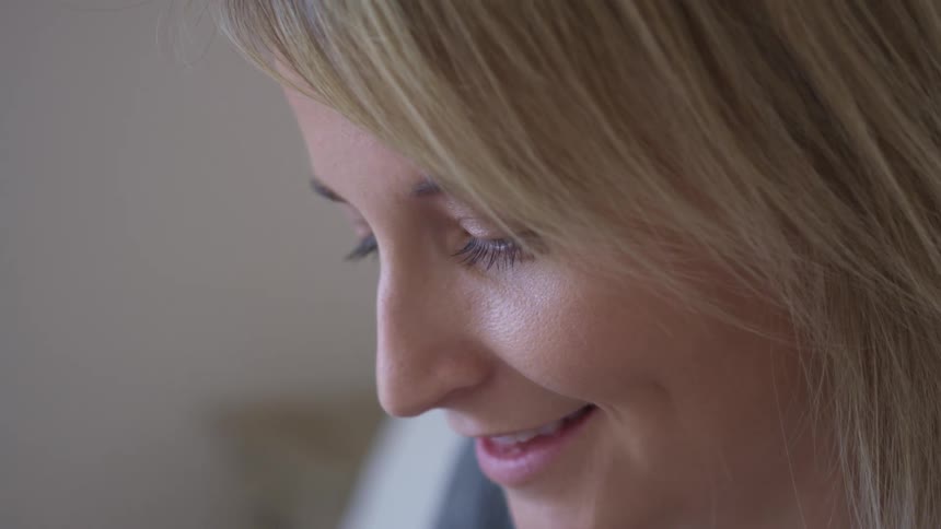 Side view of a blonde woman with dimples looks down and smiles brightly
