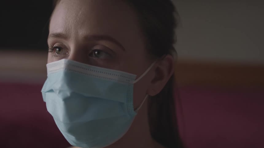 Close up of a womans face wearing a blue face mask indoors