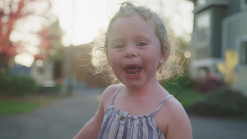 Small girl smiles and laughs on the street of the neighborhood at sunset