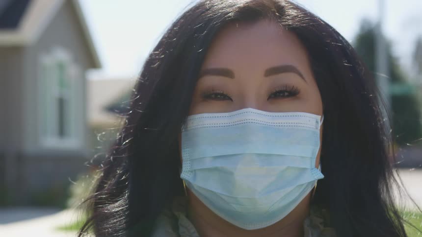 Asian woman with long black hair and a light blue mask faces the camera with eye contact