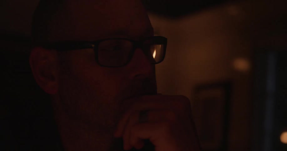 A man wearing glasses has his hand to his chin