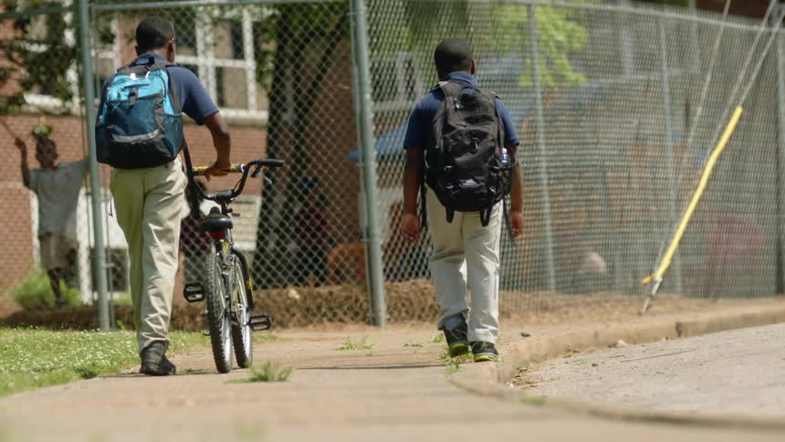 Young boys wearing backpacks push a bicycle down while walking to school