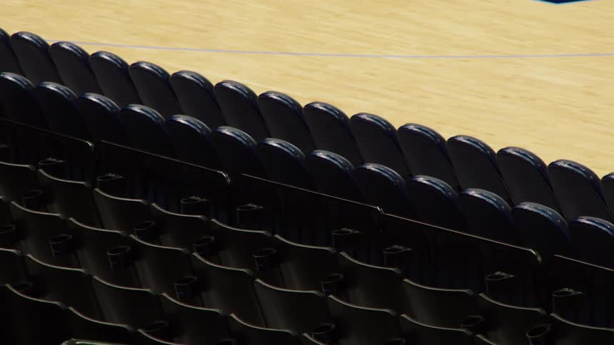 Rows of empty seats are seen lining a basket ball court within an arena