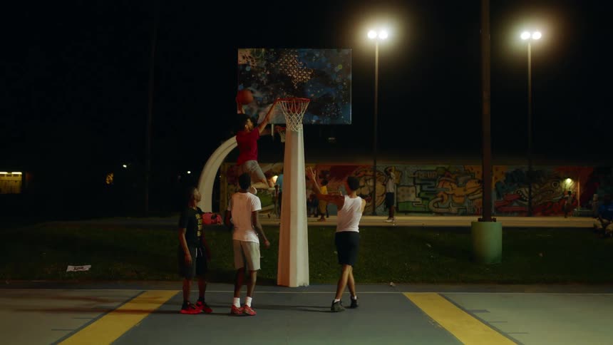 A group of men or teenagers play basketball at a public area at night