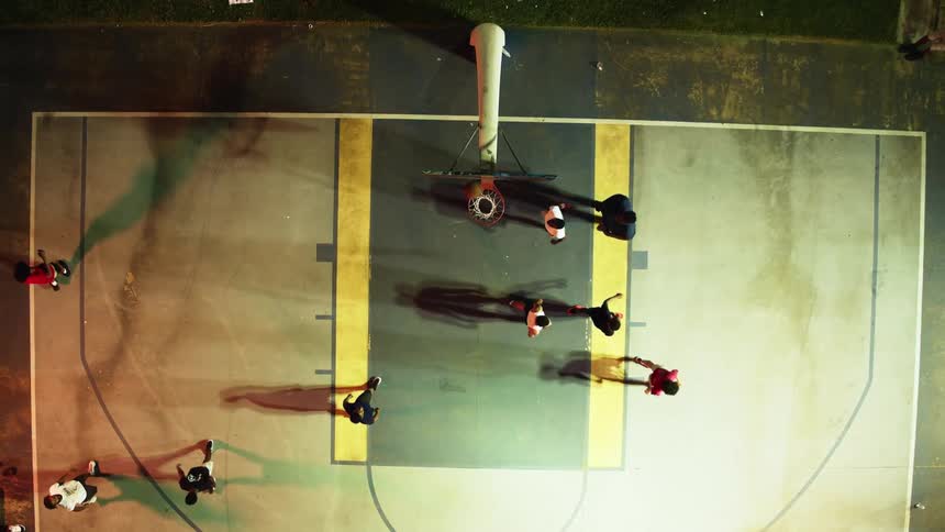 Men play basketball on yellow and black painted court bordered by green grass