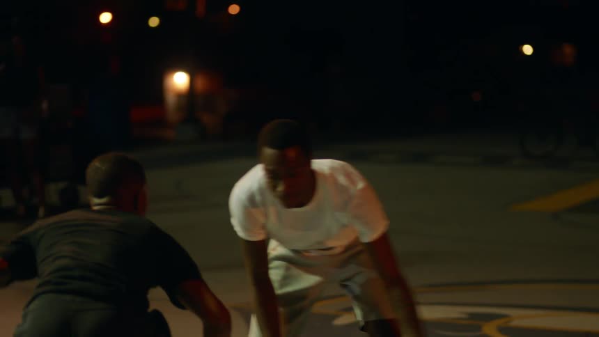 Couple of young man playing basketball in a court at night