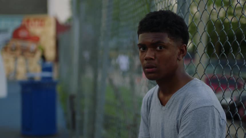 Youthsits against chain link fence bordering parking lot with parked cars