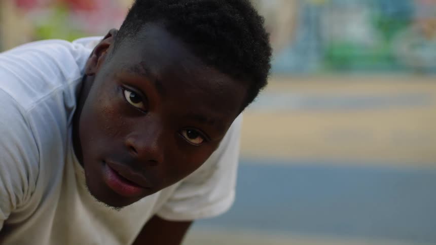 A young black man is bending over and staring at the camera