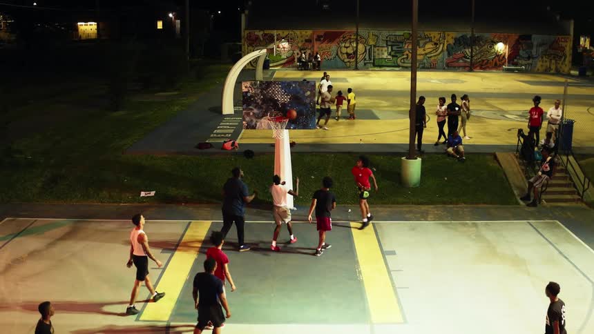 Several teams play basketball on outdoor courts at night in a park