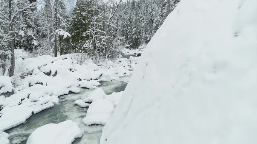 Pullback reveal of a snow covered babbling brook flowing through woods along a rugged rock ledge