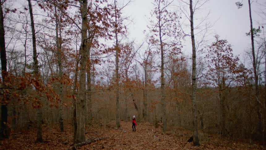 Teenage girl with a red coat and a beanie walks on the yellow leaves in the forest