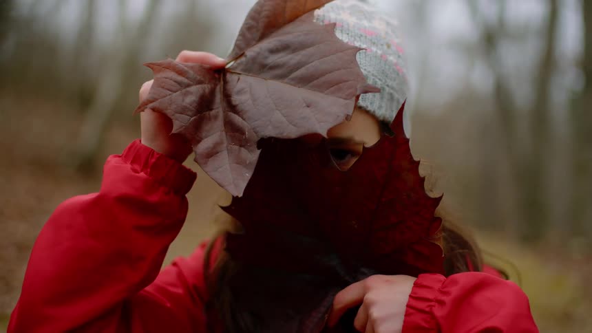 Woman stands outdoors holding large leaves to conceal her face