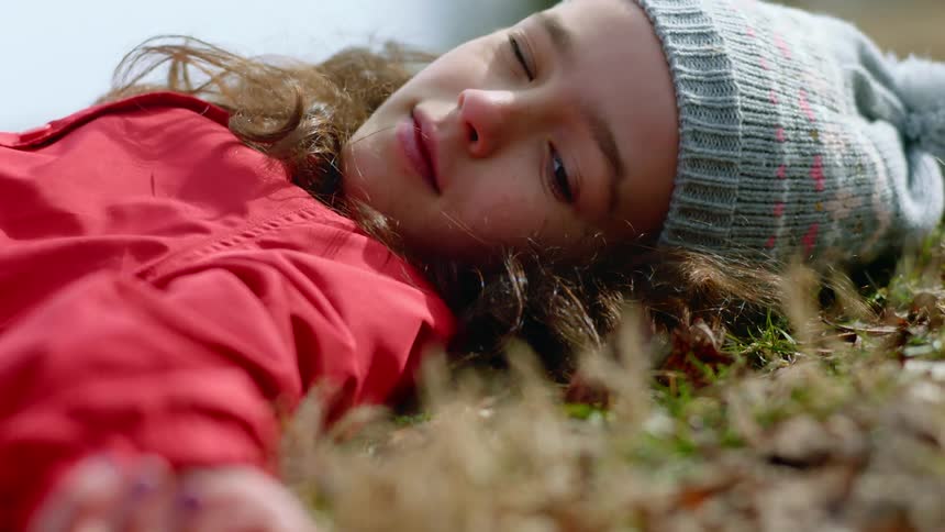 A young girl lying in leaves on the grass