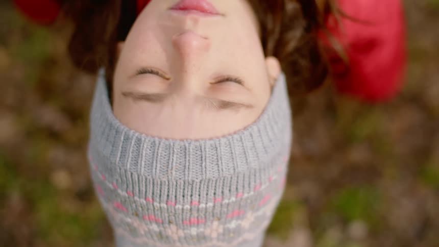 A girl leans back on a swing with her eyes closed as the wind blows through her hair