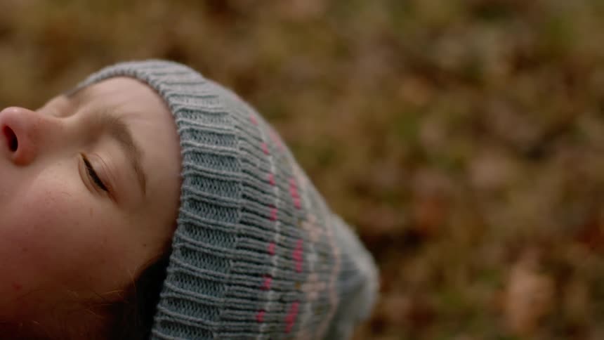 Girl with a grey beanie stands and looks up with eyes closed in the woods