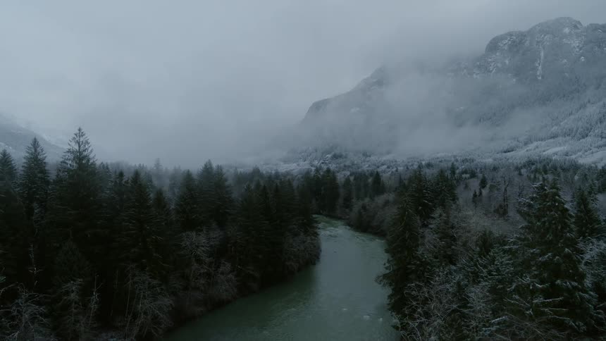 Pushing past tree tops above an icy river flowing through a misty mountain valley