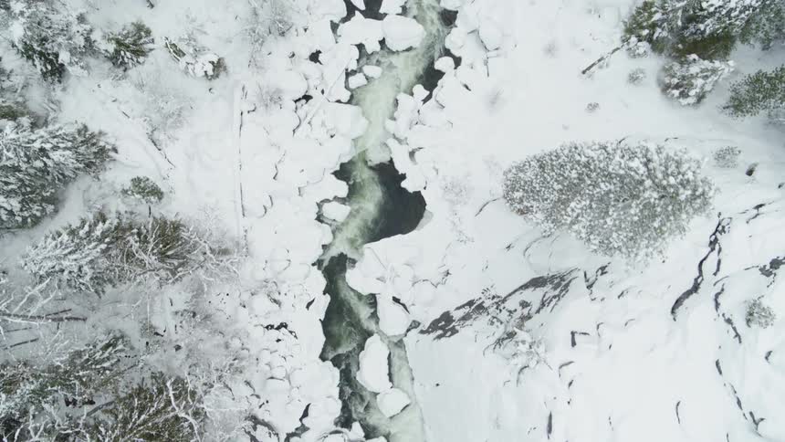 Aerial view of an icy creek carving through a snow covered mountainside