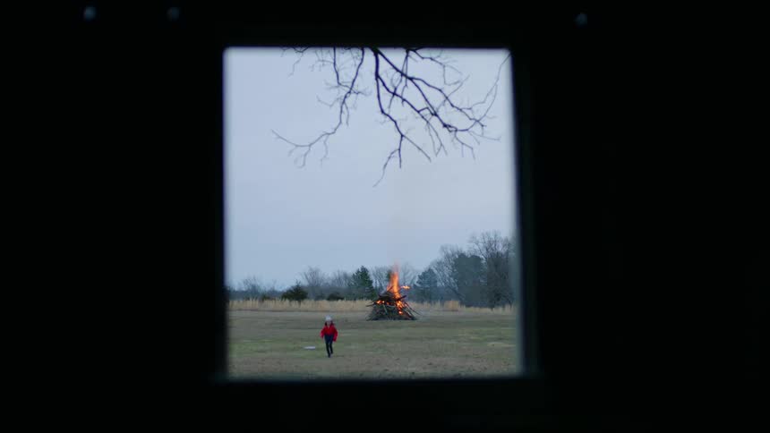 A girl running from a bonfire with trees and the sky in the background
