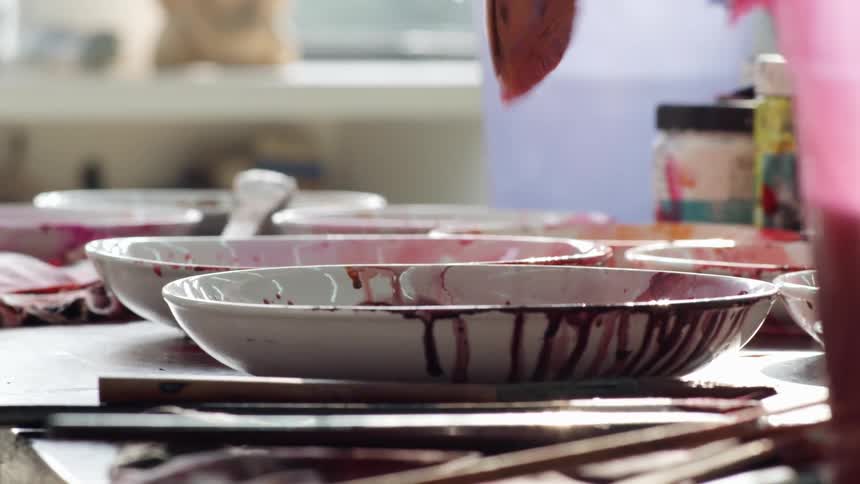 An artist mixing paint in a ceramic bowl in an art studio