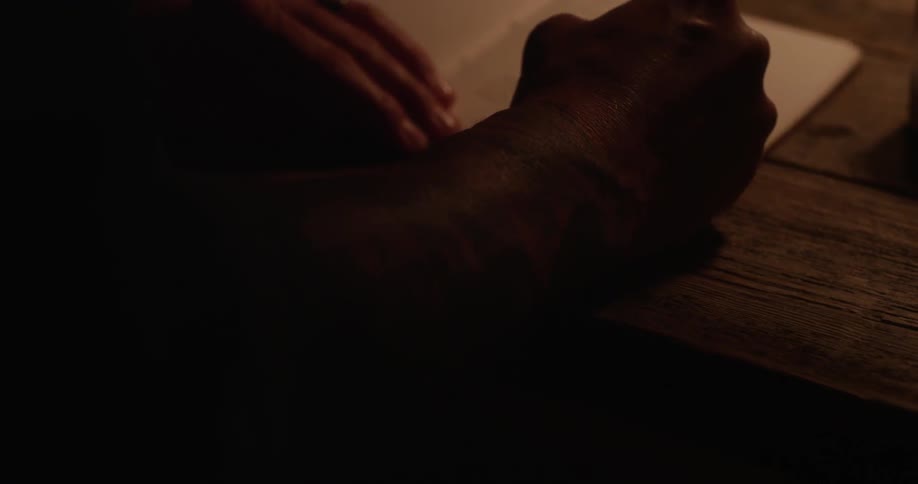 A man is writing in a notebook before drinking from a mug