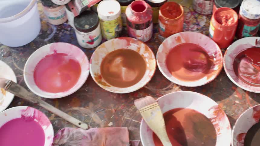 A big mess of bowls and containers of paint on a drop cloth