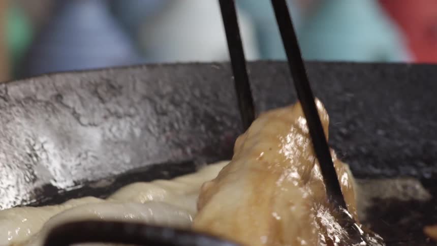 Chopsticks pick up a piece of dough frying in a cast iron pan