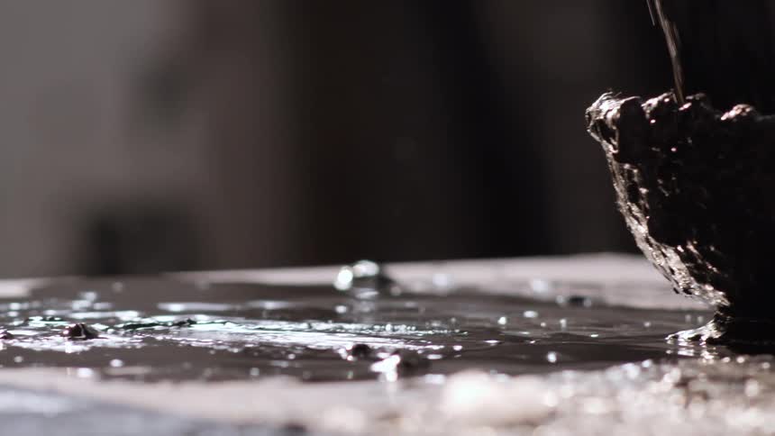 A person uses a brush to spread black paint from a bowl onto a surface