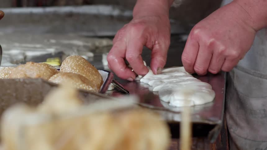 A baker cuts up a piece of dough while making rolls