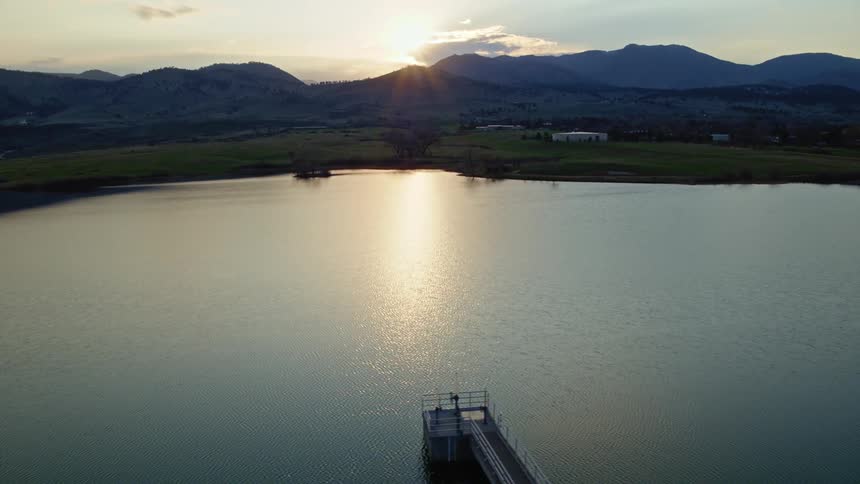 An aerial view of the water with a pier and hills in the distance