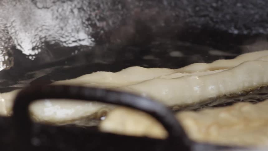 A man uses cooking chopsticks to stir chinese donuts frying in a wok