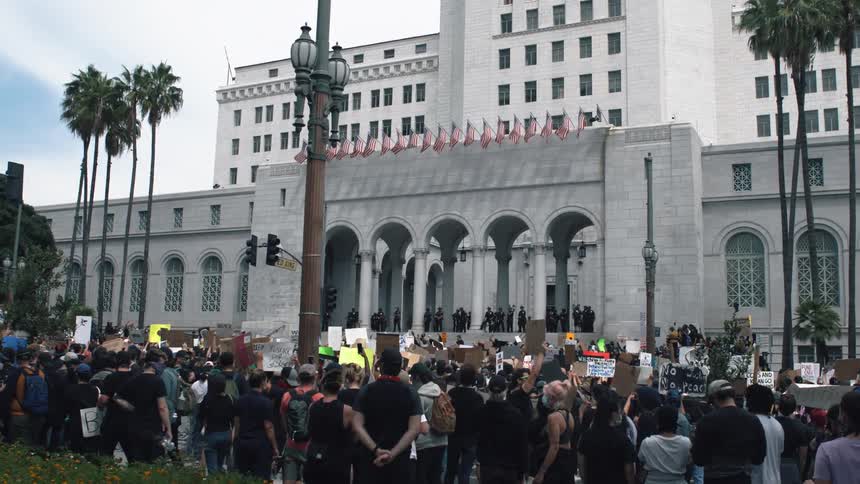 Outside of a large building there is a gathering of many demonstrators and some are holding signs