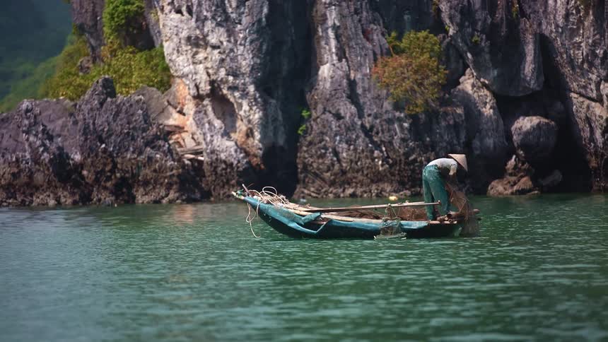 A man with a hat on a boat pulling up a fishing net on a lake