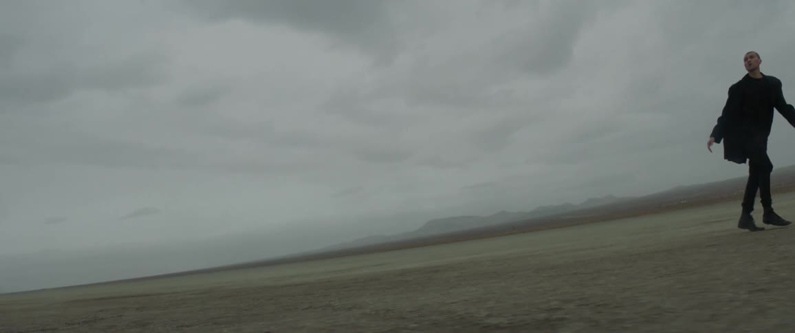 A man is walking across the desert on a cloudy day
