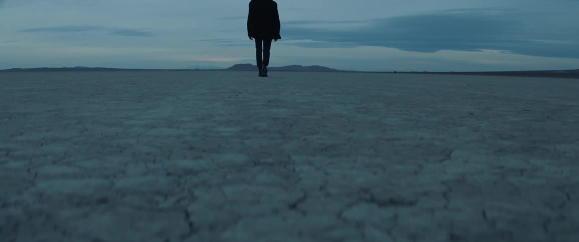 A man is walking in the desert at dusk