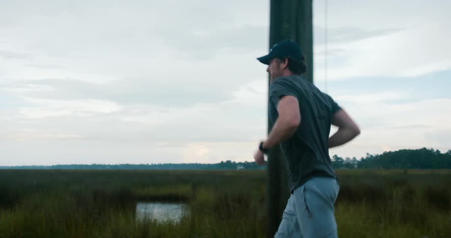 A man jogs through the countryside near a marsh on a sunny day