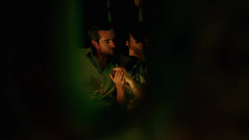 A man and woman sit together and he stroked her hair and then pulls her in and kisses her