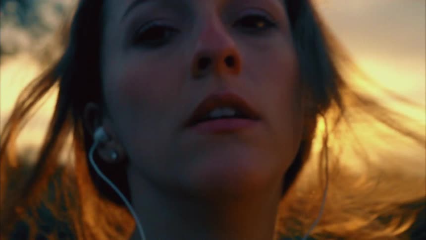 Woman with a brown ponytail faces the camera with eye contact at sunset