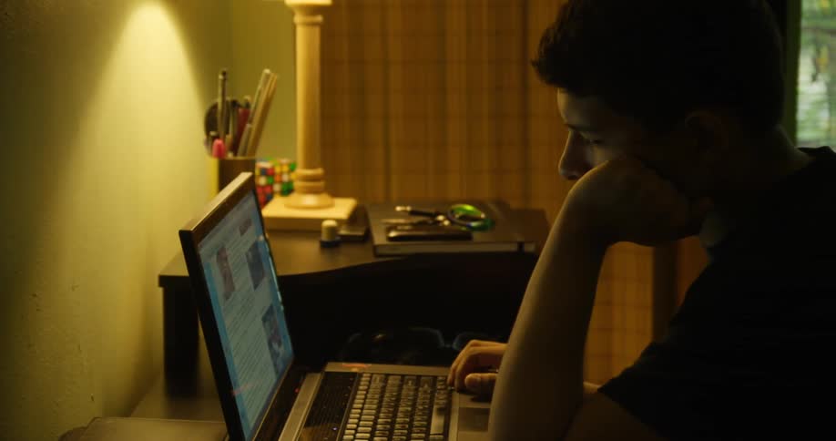 Man sits at a desk and looks at a laptop in his room