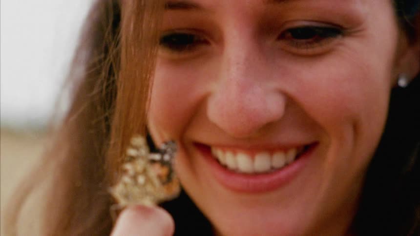 A teenage girl laughs and smiles as a butterfly rests on her finger