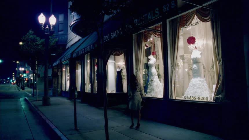 Pedestrian stops to window shop displayed gowns at night near intersection