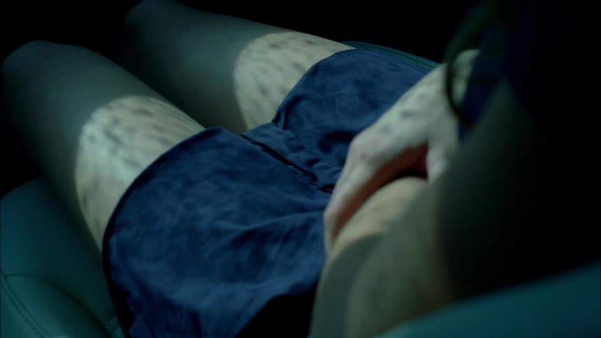 A woman sits in the passenger seat of a vehicle as the shadows of the rain drops on the windows move over her skin