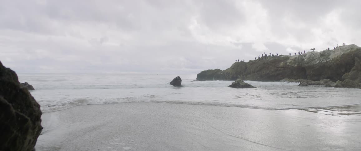Waves roll past the rocks and onto a beach