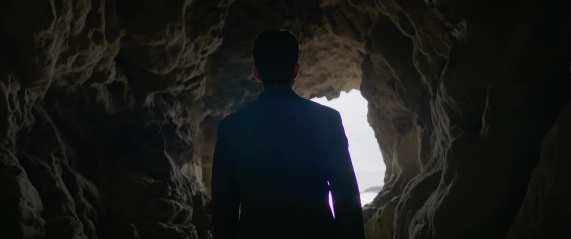 Man stands in a cave walking towards the mouth