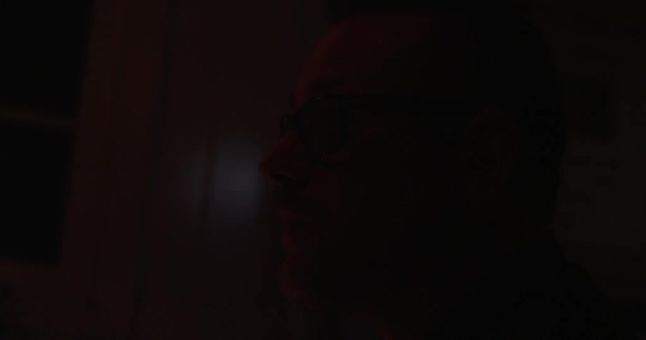 A man drinks from a mug in a dark room