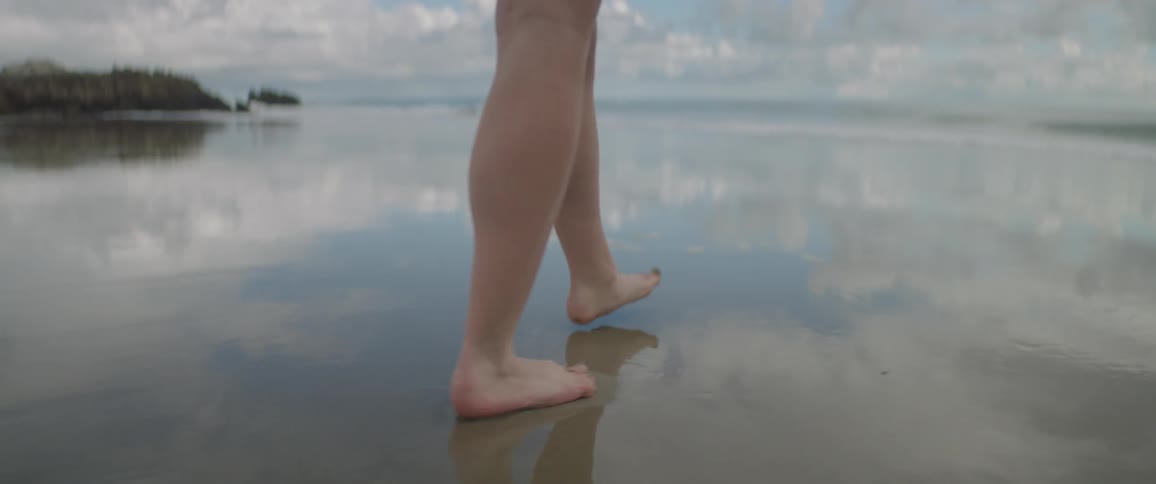 Person's bare legs walking on the sandy beach