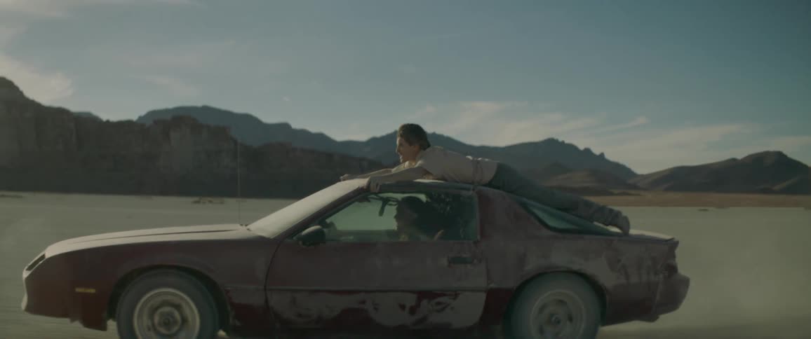 Person rides on the roof of a dusty car through the desert