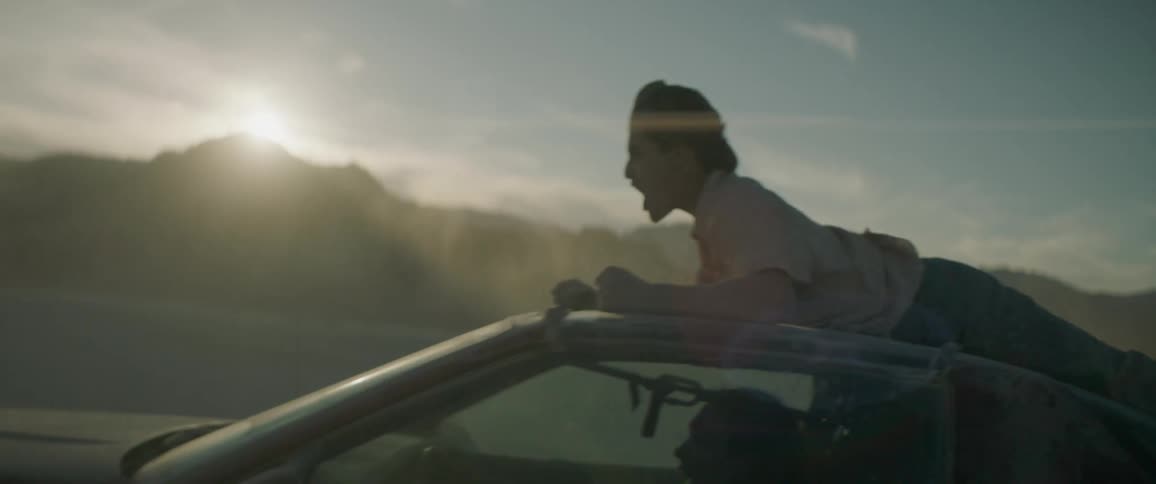 A man pumps his fist as he holds onto the roof of a moving car