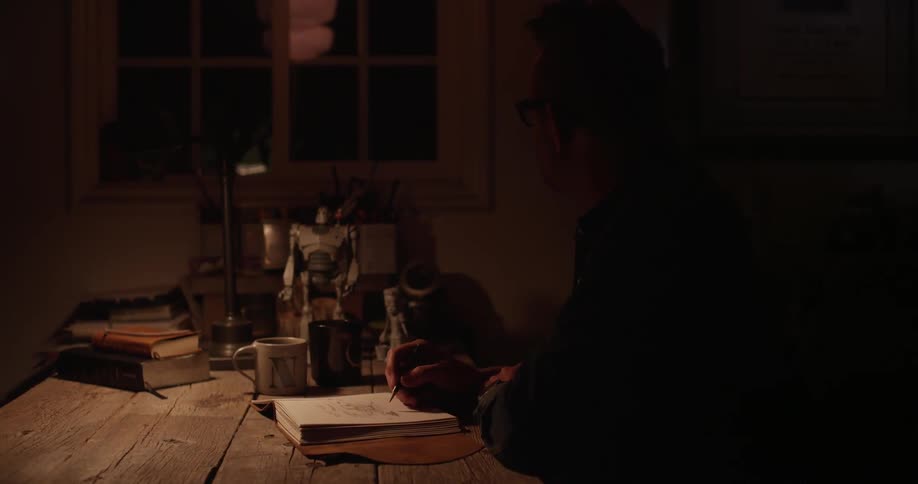 A man writes in a notebook in a dark room
