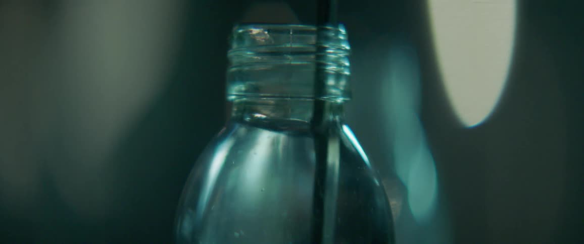 Person stirs clear liquid in a glass bottle