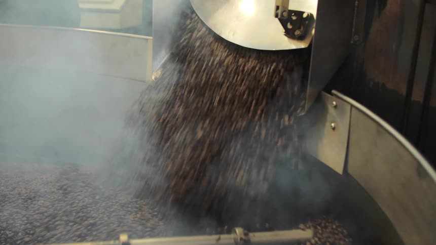 Coffee beans pour into a large take where they are stirred by an agitator